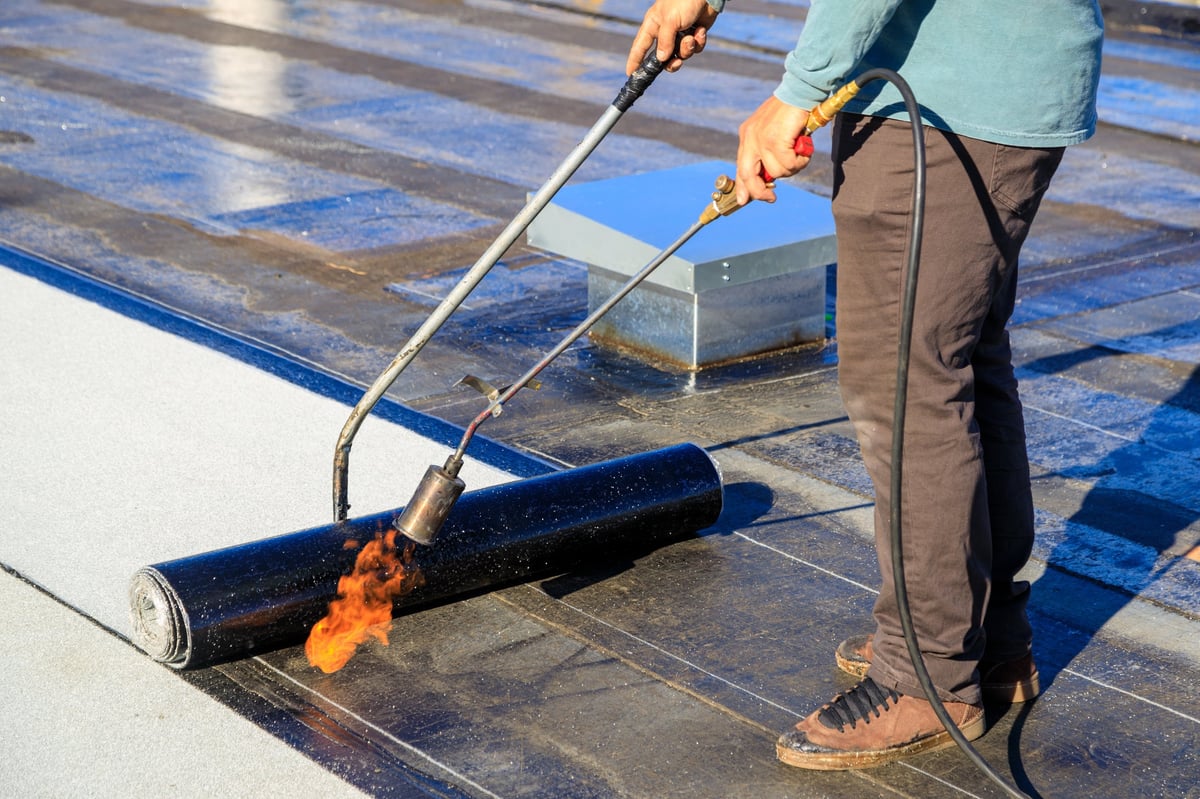 Roofer sealing a flat roof membrane with a torch